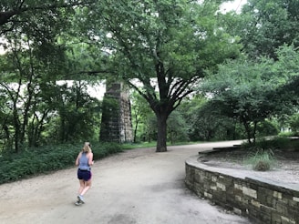 A cheerful woman jogging outdoors in a lush park setting.