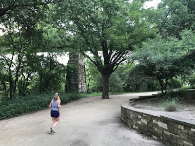 A candid moment of a woman jogging through a leafy neighborhood path.
