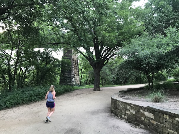 A cheerful woman jogging outdoors in a lush park setting.