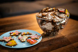 A rustic wooden table displaying an assortment of cookies and fudge in pastel wrappers.