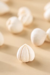A close-up of several dried lotus seeds scattered on a smooth, beige surface. Each seed has a creamy white color and a hard outer shell with distinctive seam lines. The focus is sharp on one central seed with a blurred background, giving a sense of depth.