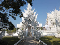 The serene white temples and rolling hills of Chiang Rai under a bright blue sky.
