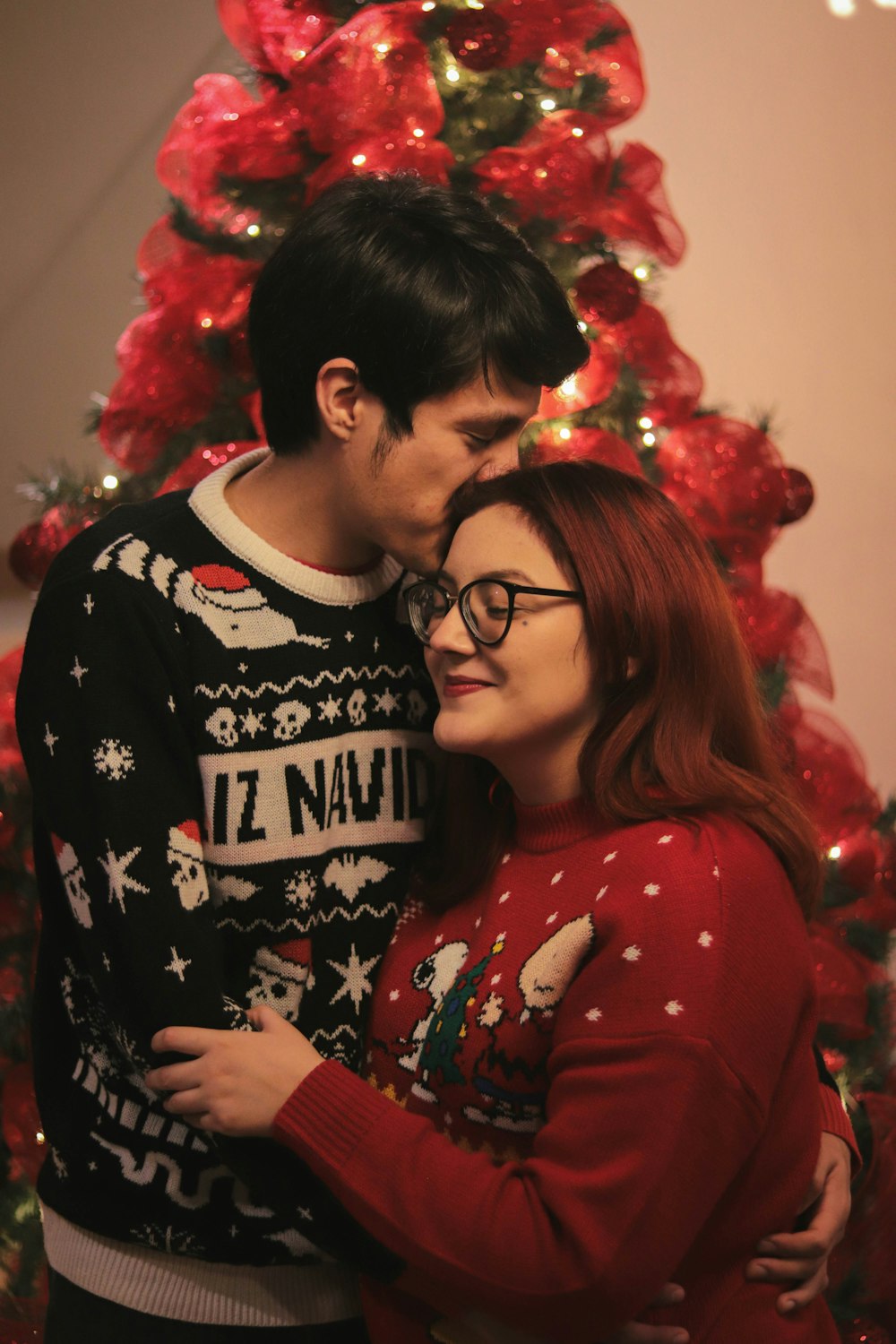 a man and a woman standing in front of a christmas tree