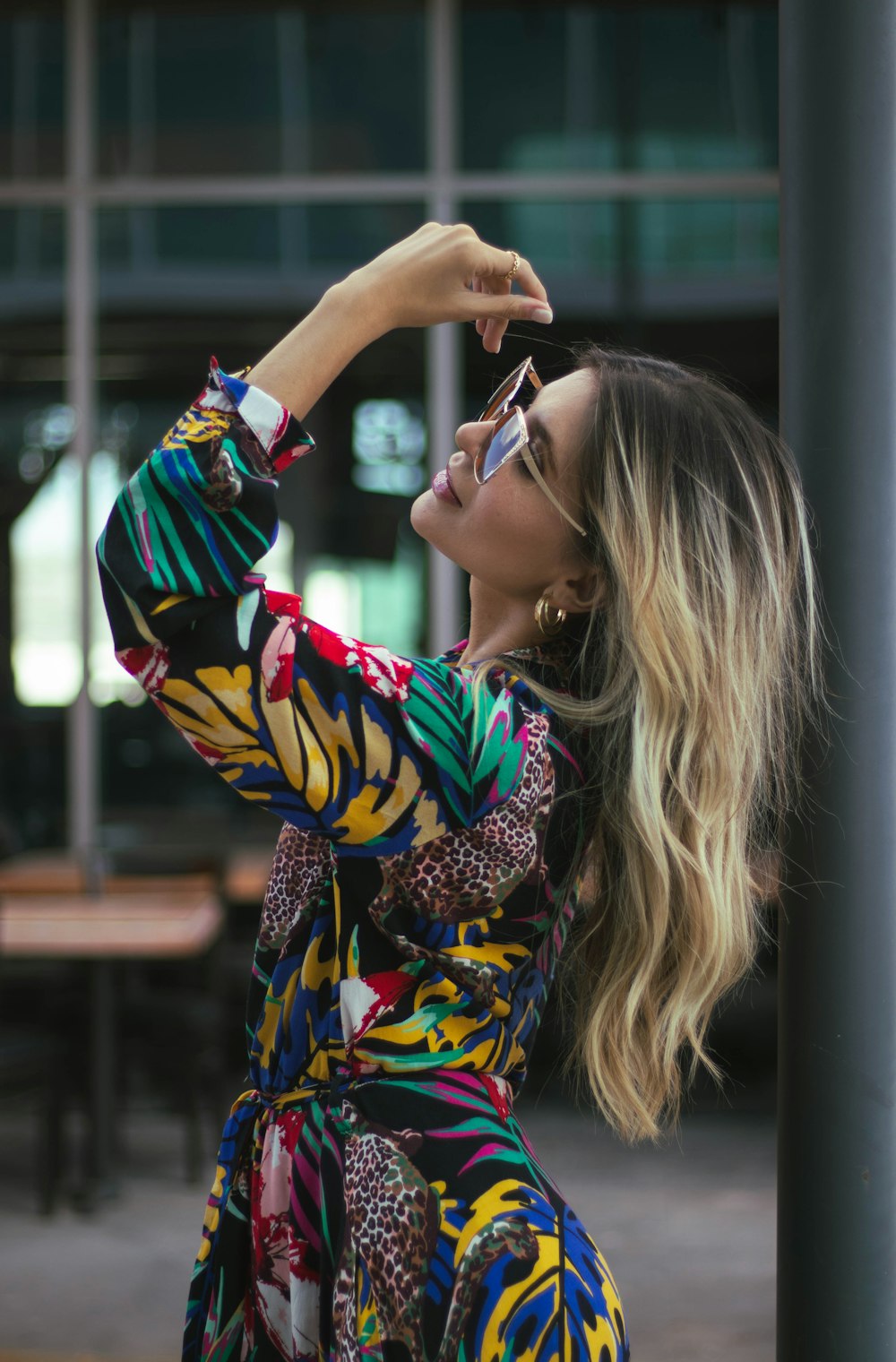 a woman in a colorful dress leaning against a pole