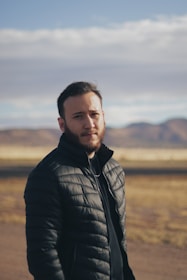 Close-up of a man adjusting his outdoor jacket with mountains in the background under a clear sky.