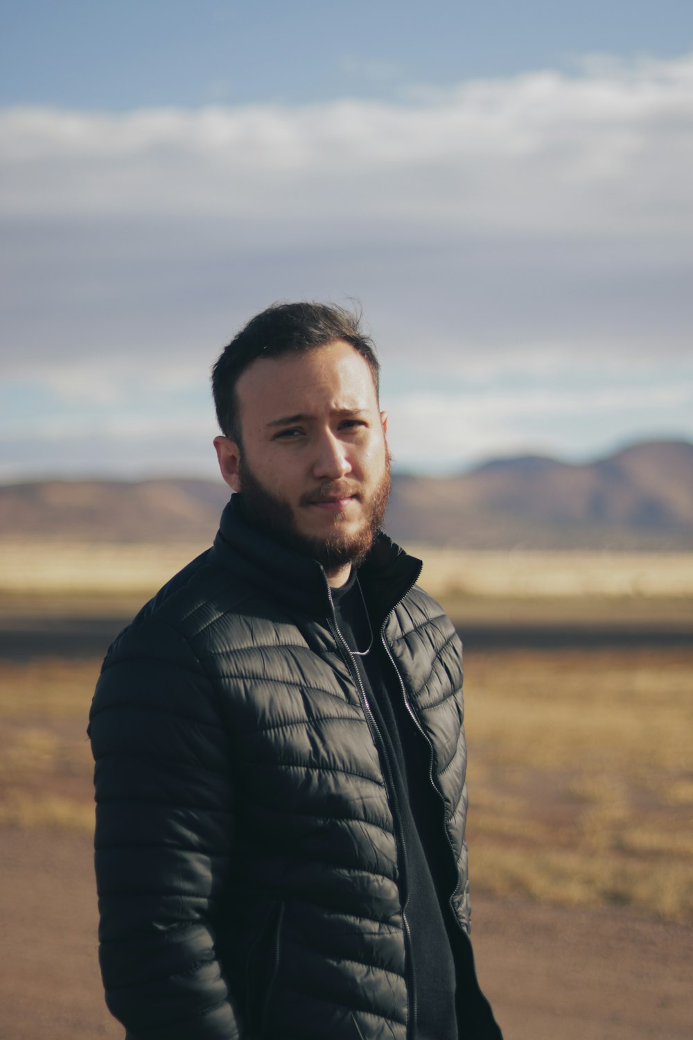 a man in a black jacket standing in a desert