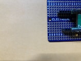 A blue prototyping breadboard with various holes arranged in a grid pattern is partially visible. Markings include numbers along the edges and the word 'ELECTRICAL' printed in white letters. The background is a plain beige surface.