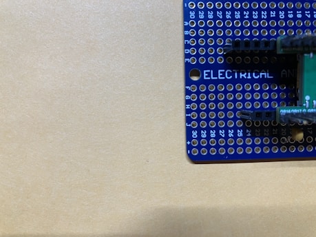 A blue prototyping breadboard with various holes arranged in a grid pattern is partially visible. Markings include numbers along the edges and the word 'ELECTRICAL' printed in white letters. The background is a plain beige surface.
