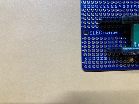 A blue prototyping breadboard with various holes arranged in a grid pattern is partially visible. Markings include numbers along the edges and the word 'ELECTRICAL' printed in white letters. The background is a plain beige surface.