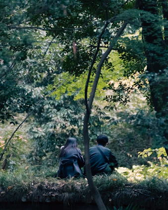 Two people sitting close together on a wooden chair surrounded by lush greenery, sharing a heartfelt conversation in nature.