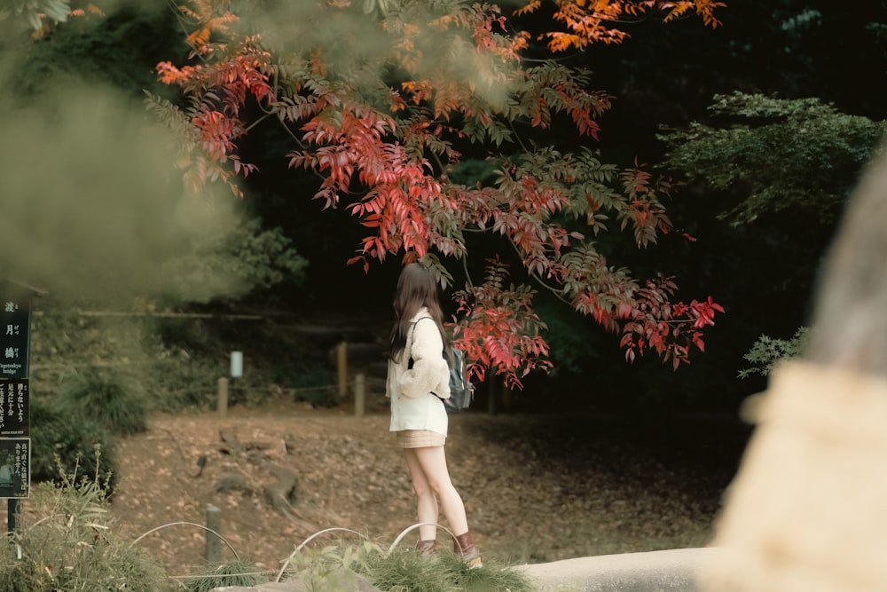 a woman standing under a tree with red leaves