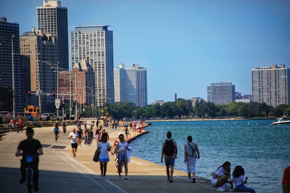 a group of people walking down a sidewalk next to a body of water