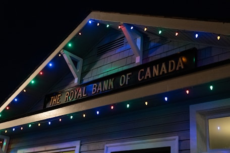 A building facade displaying 'The Royal Bank of Canada' sign, adorned with colorful string lights in blue, red, green, and yellow hues.