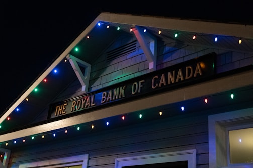 A building facade displaying 'The Royal Bank of Canada' sign, adorned with colorful string lights in blue, red, green, and yellow hues.
