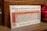 A vintage poster from The Royal Bank of Canada showing a savings chart that projects potential worth at age 65 based on current age and monthly savings. The chart includes a list of ages from 20 to 50, and various monetary goals ranging from $5,000 to $40,000. The poster is displayed on a wooden stand with decorative red flowers beside it.