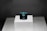 A dark blue rectangular gemstone is placed on a raised white platform against a dark background. The gem is faceted and exhibits a deep, rich hue, with light reflecting off its polished surfaces.