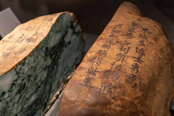A large stone slab with one side featuring intricate black calligraphy on a smooth, brown surface, while the other side displays a raw, greenish texture resembling jade or marble.