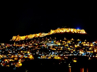 A sprawling walled city under a twilight sky, with shadowy figures lurking beyond the walls.