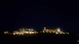 Nighttime illumination highlighting the architectural details of a fortress.