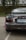 The rear view of a dark gray sports car with a prominent spoiler. Decorative stickers are visible on the back, including a character and the phrase 'DRIVE SAFE'. The car has round tail lights and is parked on an asphalt road next to some greenery.