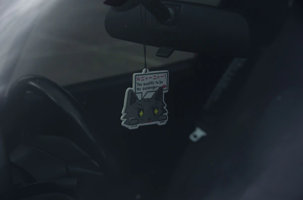 A vibrant automotive premium air freshener hanging inside a modern electric car, complementing the Revintec charger cover.