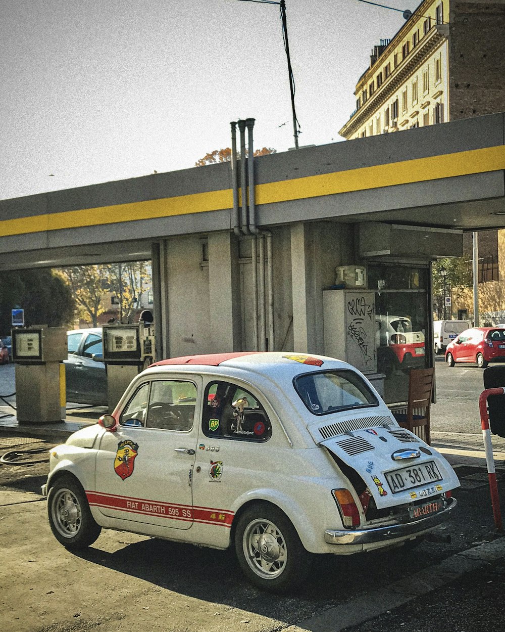 a small white car parked next to a gas station