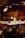 Warm, glowing lights hang from the ceiling in a cozy, festive market setting. Decorative ornaments add to the holiday atmosphere, with people mingling in the background, suggesting a busy and lively environment.