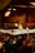 Warm, glowing lights hang from the ceiling in a cozy, festive market setting. Decorative ornaments add to the holiday atmosphere, with people mingling in the background, suggesting a busy and lively environment.