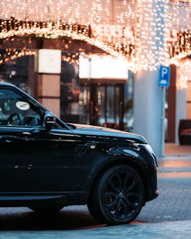 A sleek black SUV parked curbside at a bustling airport terminal under bright Las Vegas lights.