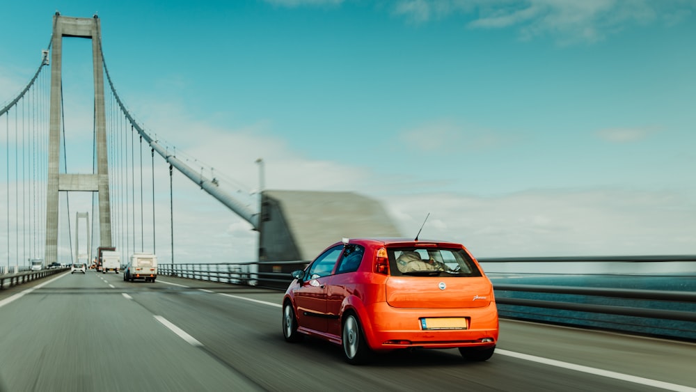 Un coche naranja conduciendo por un puente con un puente al fondo