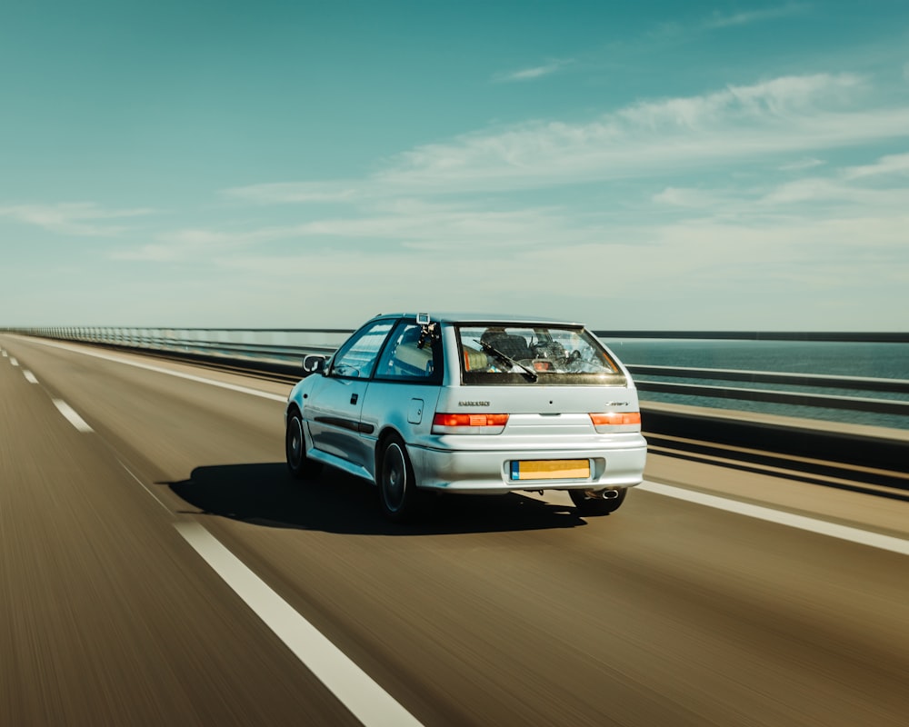 a white car driving down a highway next to the ocean