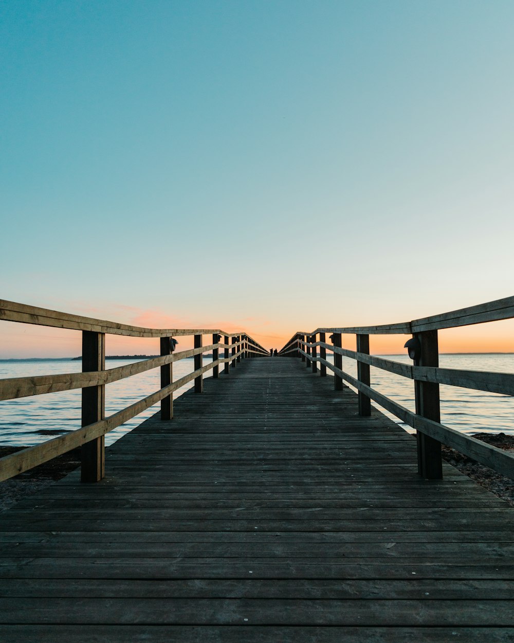 a wooden pier with a view of the ocean at sunset