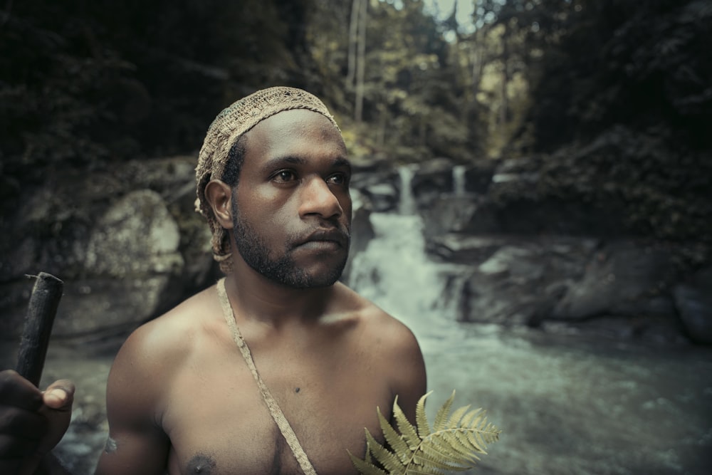 a shirtless man holding a stick in front of a waterfall