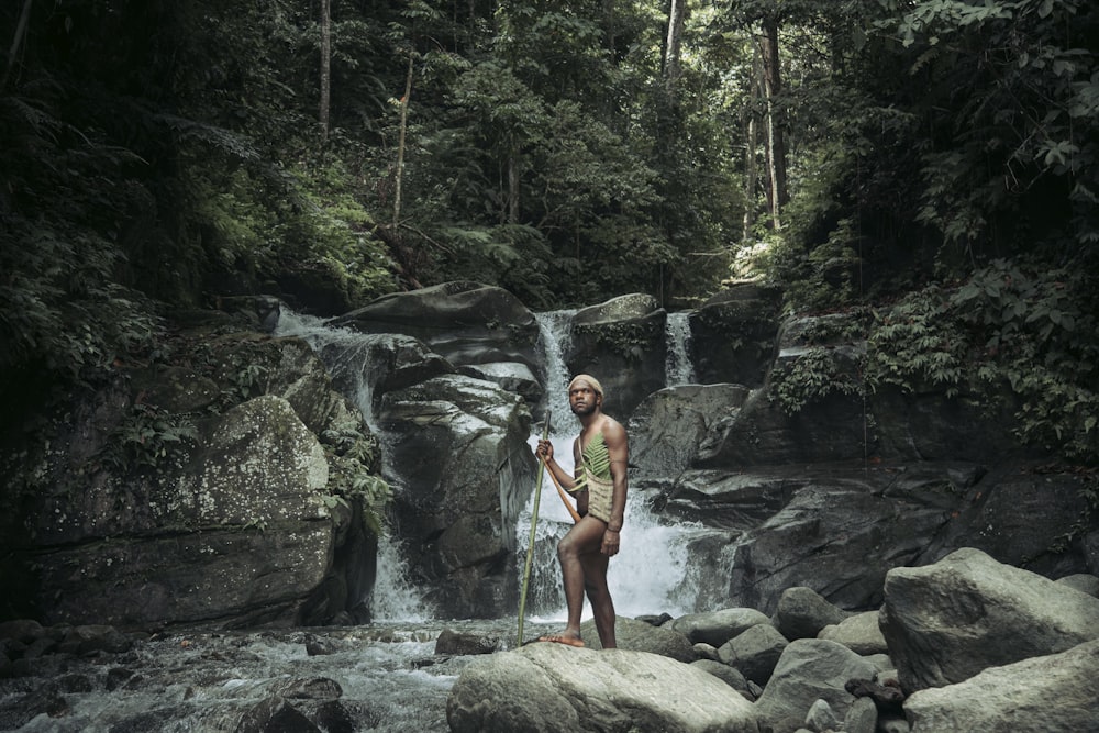 a man standing on rocks in front of a waterfall