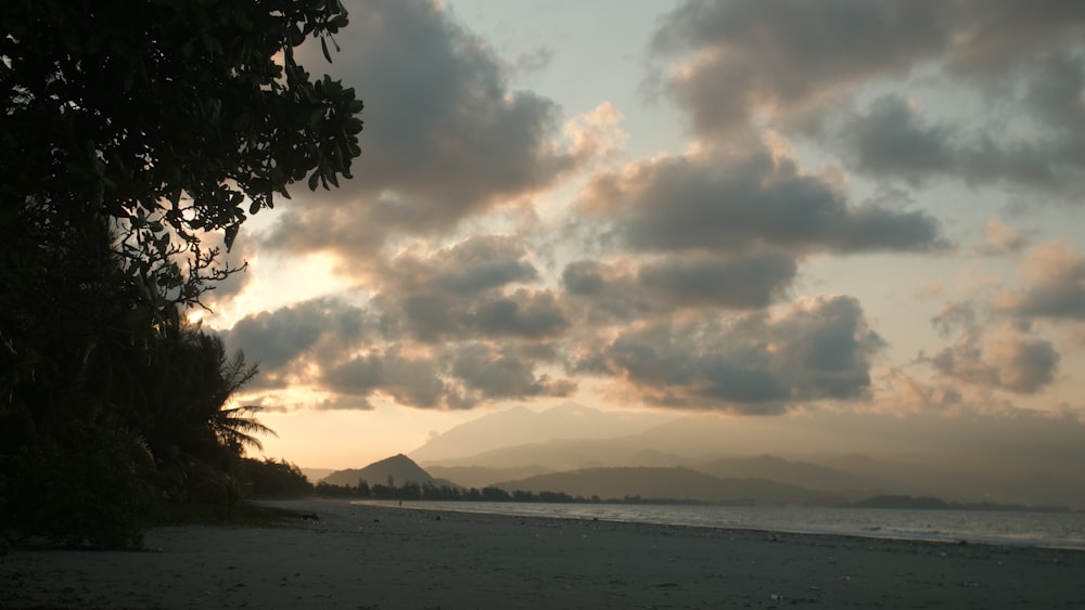 the sun is setting on the beach with clouds in the sky