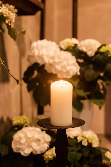Softly lit candle beside a delicate bouquet of white lilies on a muted blue background.