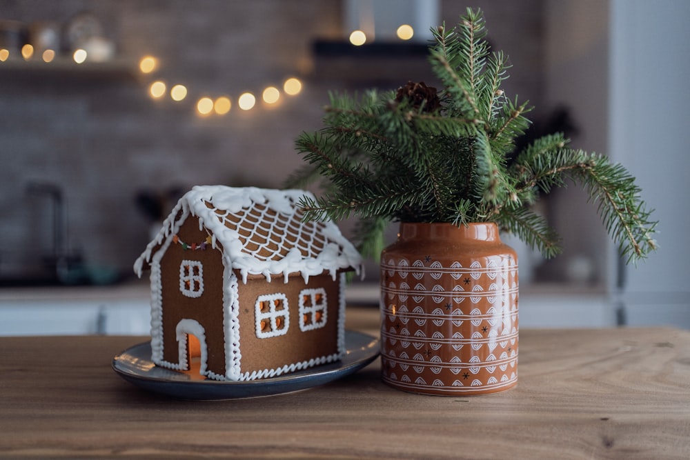 a gingerbread house sitting on a plate next to a potted plant