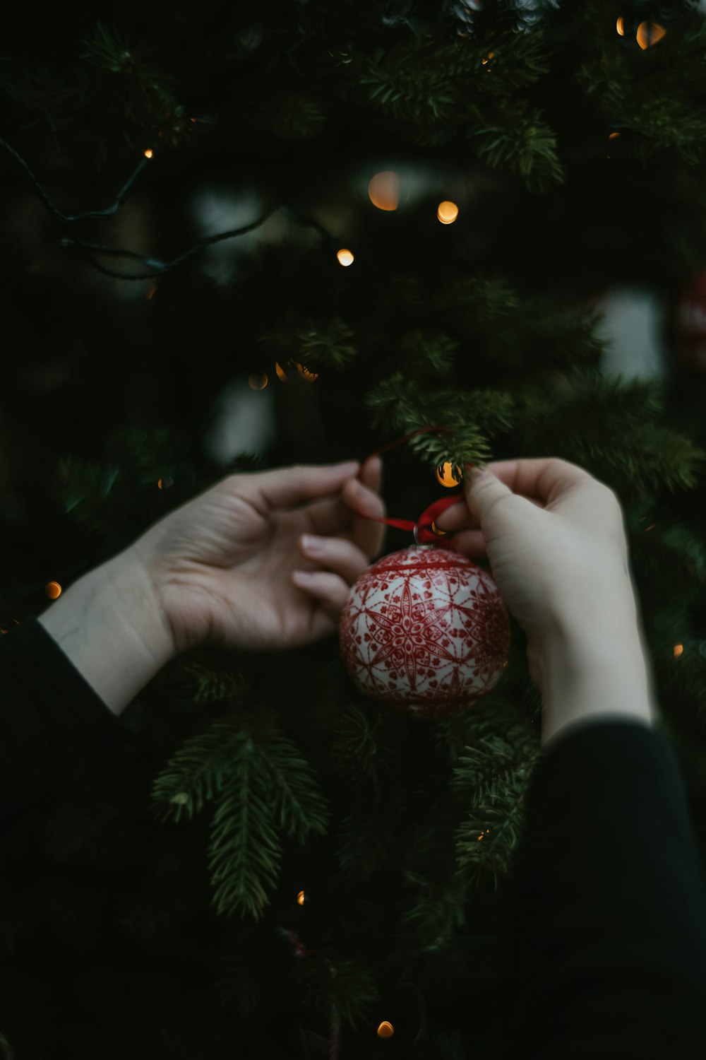 two hands holding a red ornament on a christmas tree
