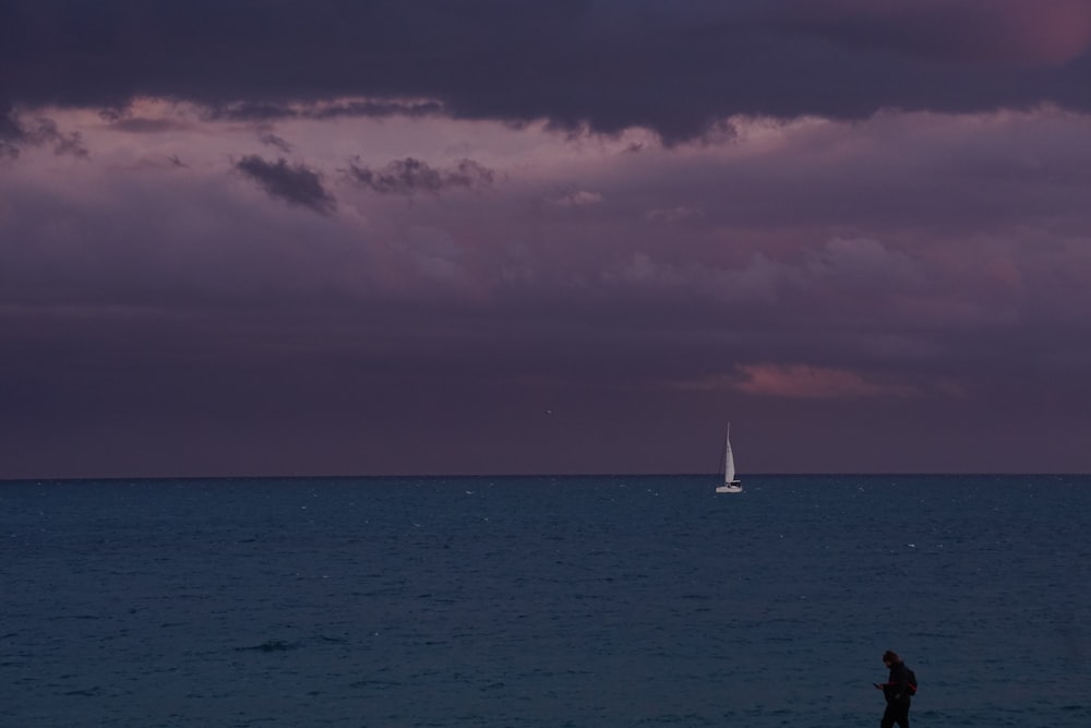 a person standing on a beach watching a sailboat