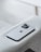 A modern smartphone with a sleek design and three camera lenses on the back is placed on a light gray fabric surface. The device features a recognizable apple logo.