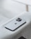 A modern smartphone with a sleek design and three camera lenses on the back is placed on a light gray fabric surface. The device features a recognizable apple logo.