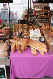 A modern food market stall showcasing an array of handmade breads and pastries with textured parchment wrapping.