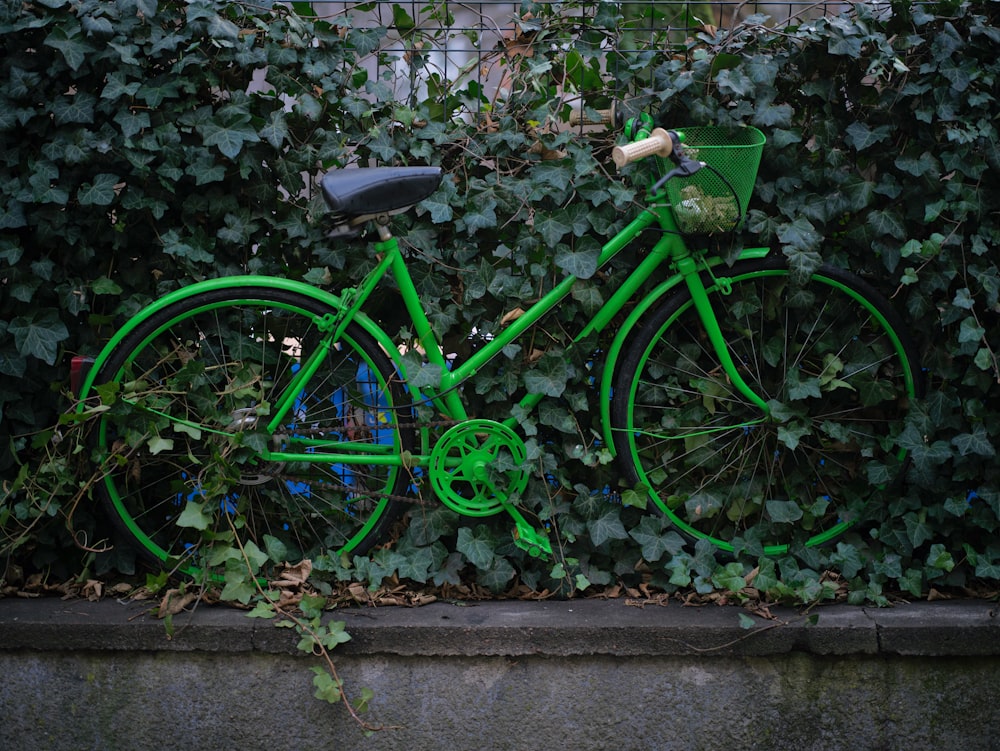 a green bicycle is parked in front of a wall of ivy