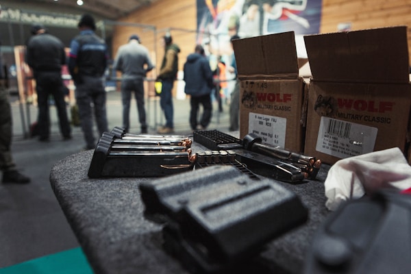 A table is covered with ammunition, including magazines and various bullets. Boxes labeled 