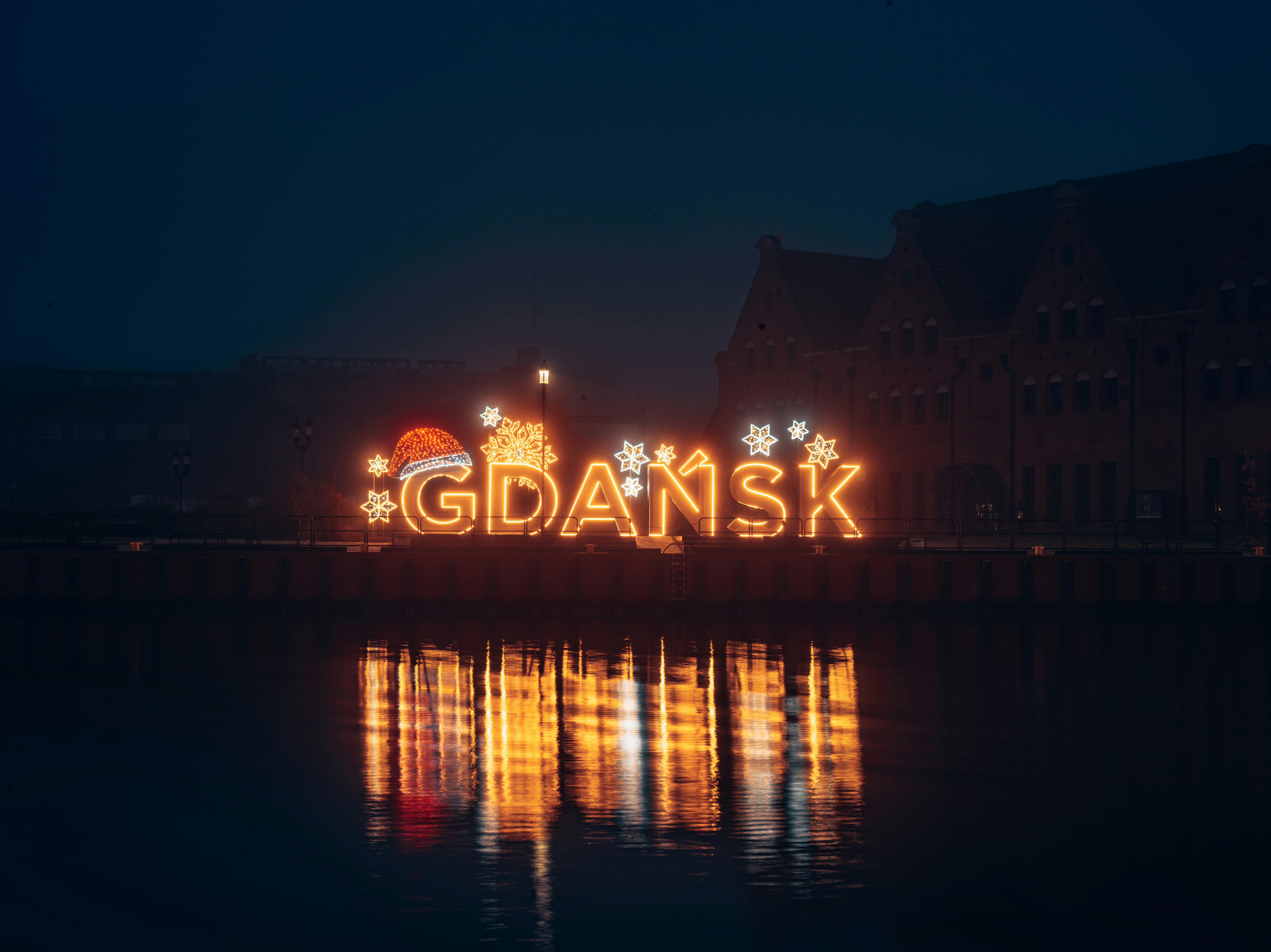 a lighted sign that says gdansk in front of a body of water
