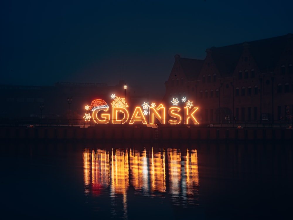 a lighted sign that says gdansk in front of a body of water