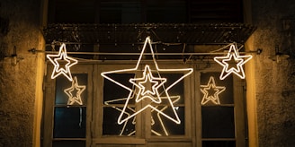 Five glowing star-shaped lights are arranged across a wooden door with barred windows. The surrounding area includes a rustic wall with textured surfaces.