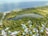 An aerial view of a coastal area featuring a large, lush green forest surrounding a serene pond. Residential houses with colorful rooftops are visible along with a shoreline bordered by the ocean.