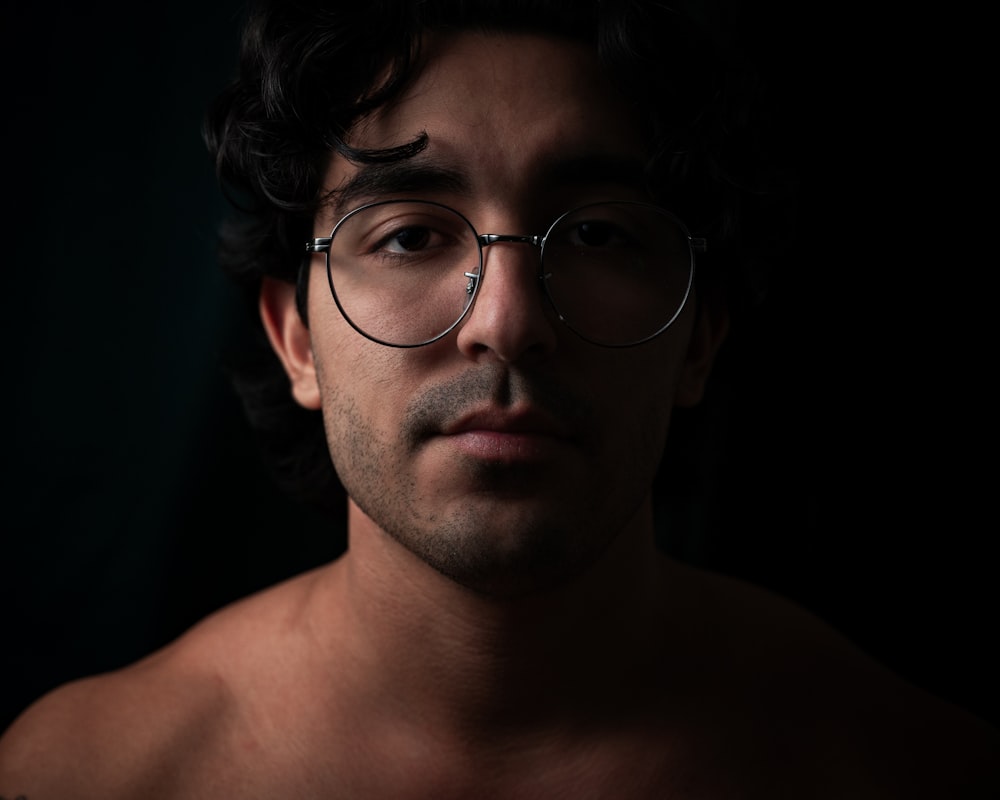 a shirtless man wearing glasses in the dark