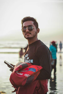 A stylish man wearing a District Beach jacket standing by the waterfront at sunset, blending cityscape and coastal elements.